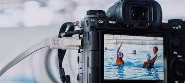 Imagen de uso de la cámara montada en un tripié y conectada a un cable LAN que hace capturas a un partido de waterpolo con una imagen en vivo que se muestra en el monitor LCD