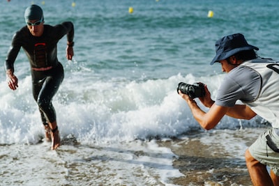 Imagen de uso de un hombre sujetando la cámara para tomar capturas a un triatleta que sale corriendo del mar