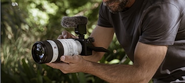 Foto de un hombre grabando un video con un micrófono conectado a la cámara