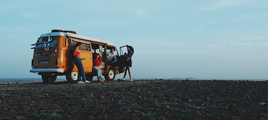 Imagen de ejemplo de cuatro hombres y mujeres charlando alrededor de una autocaravana naranja