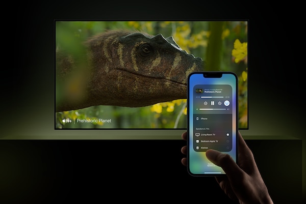 TV instalada en la pared con una captura de pantalla de una cabeza de dinosaurio y una mano que sostiene un smartphone